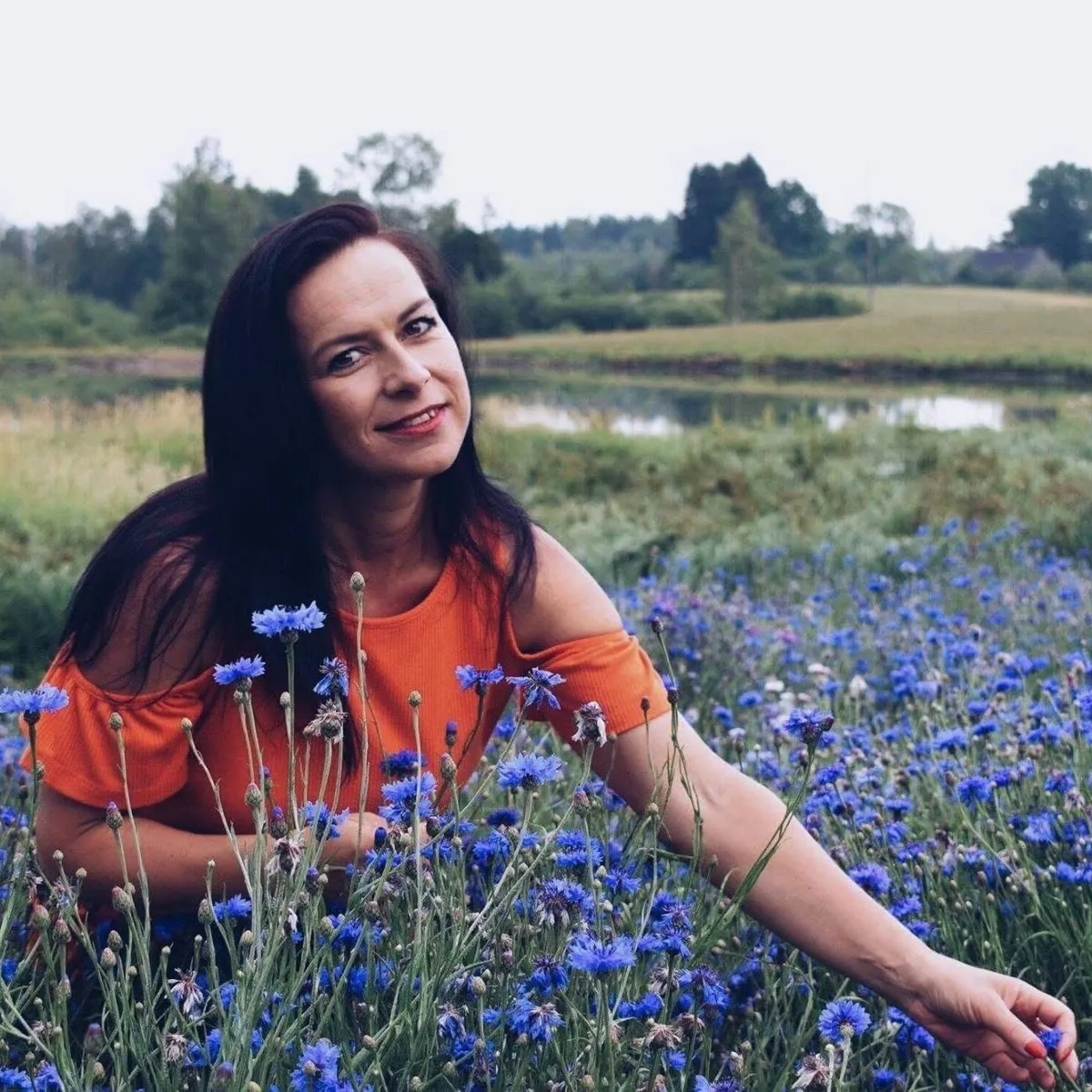 Smaidoša sieviete ar gariem, tumšiem matiem rudzupuķu laukā