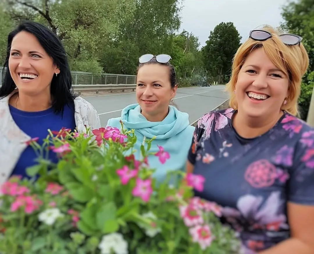 Salona „Skaistuma serviss” meistares smaida, priekšplānā rozā puķes